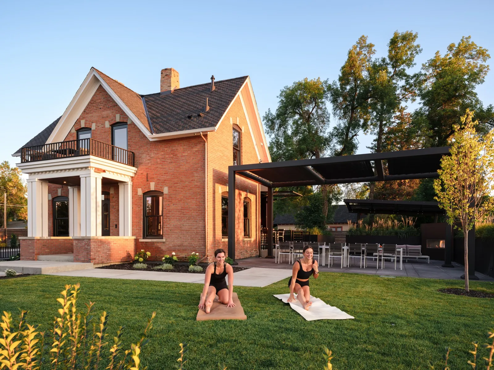 Two guests practicing yoga on the lawn beside historic Rouse House and its garden terrace